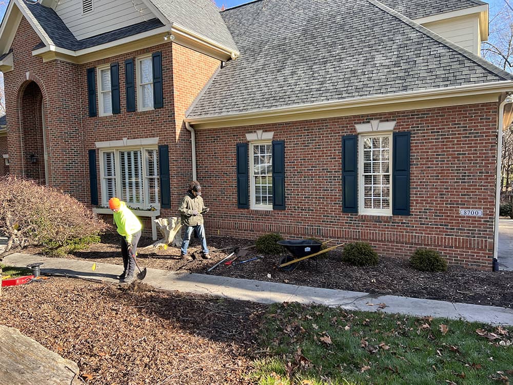 professionals puting down mulch in front of brick home